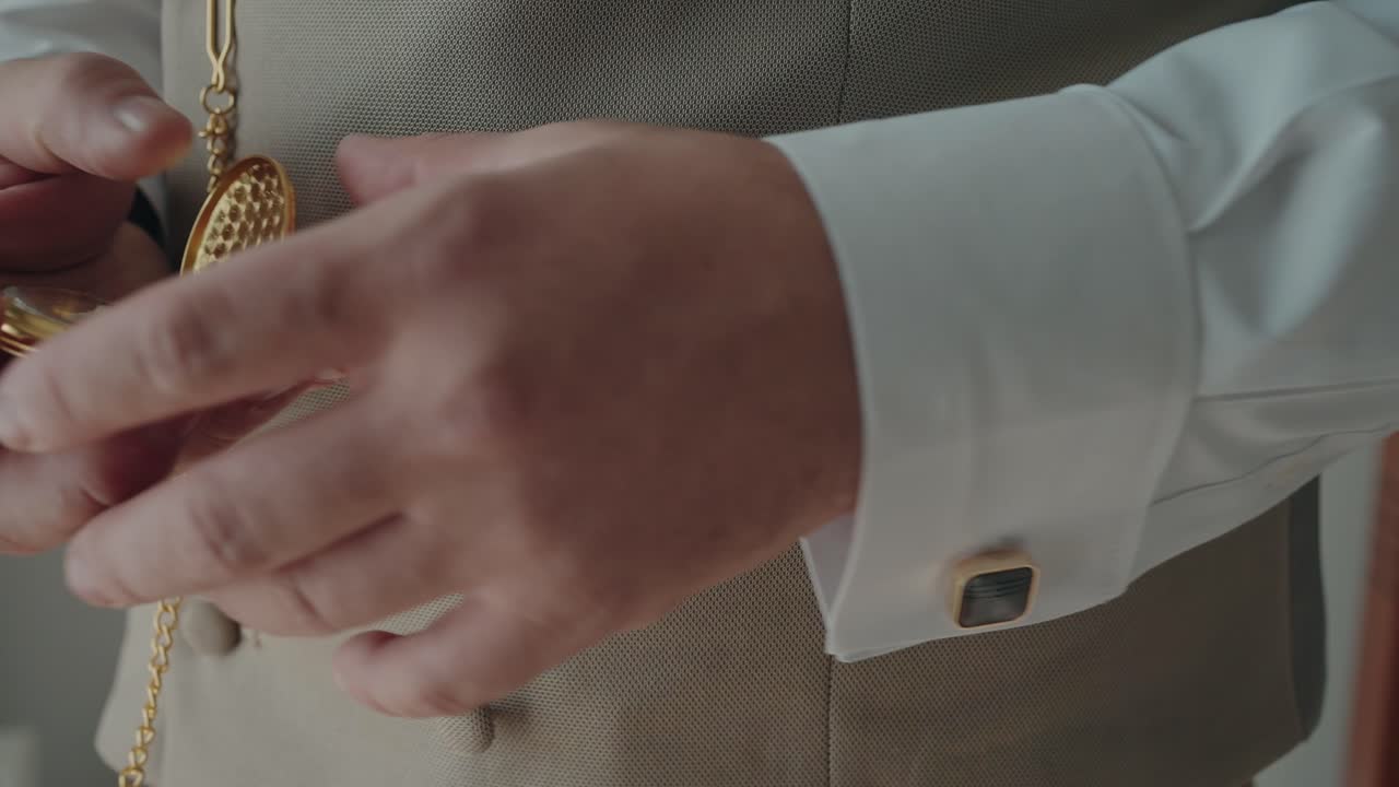 Closeup of person in beige waistcoat and white shirt using gold chain pocket watch