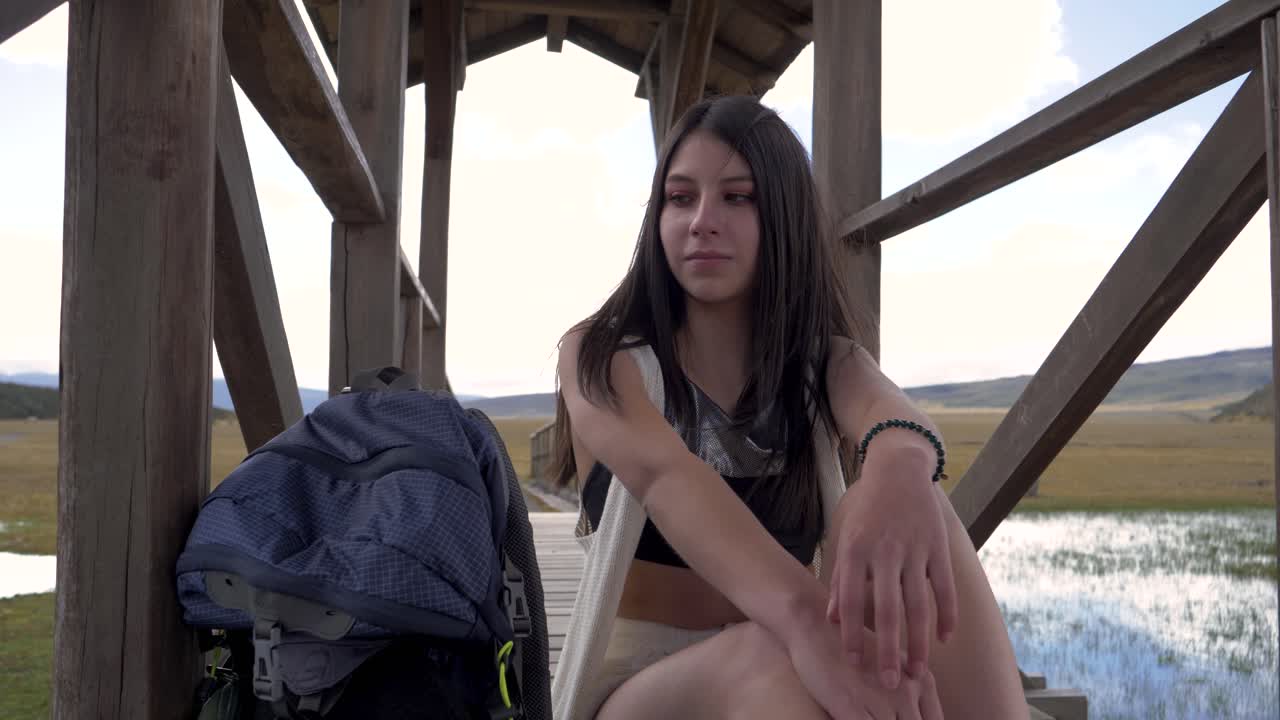 Woman sits on bridge looking out and smiling fixing hair enjoying cotopaxi national park