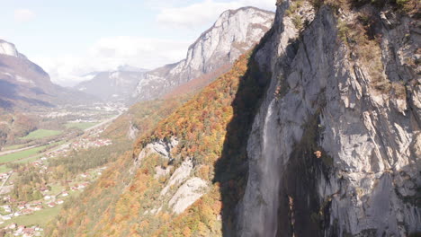 flying towards a beautiful small waterfall spawning a rainbow with a colorful forest in autumn in the background