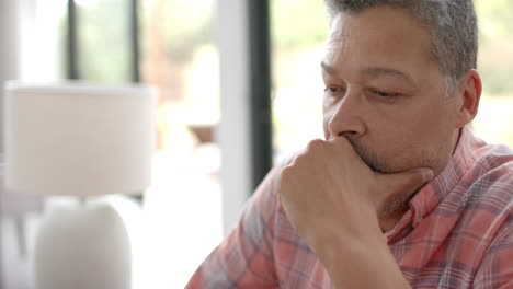 Worried-senior-biracial-man-sitting-thinking-in-living-room-at-home,-copy-space,-slow-motion