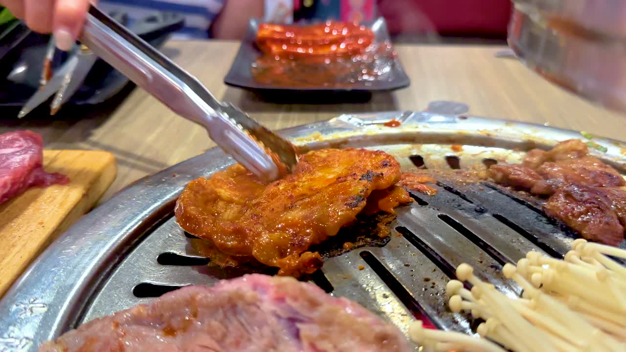 Grilled meat and mushrooms sizzle on a Korean BBQ grill in a vibrant Bangkok setting, showcasing culinary techniques and flavors