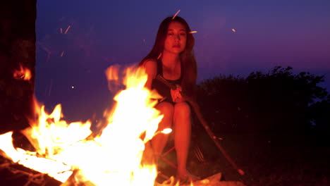 asiatic chinese young woman model girl putting wood on bonfire while camping at night