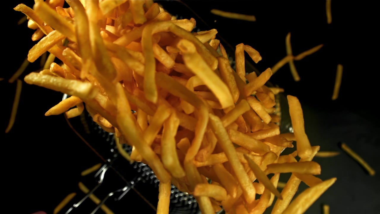 Läckra gyllene pommes frites faller i slow motion från en frityrkorg