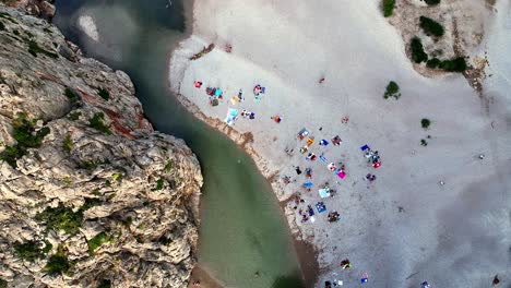 rising drone top shot of some people with blankets on the beach in a lagoon on mallorca.