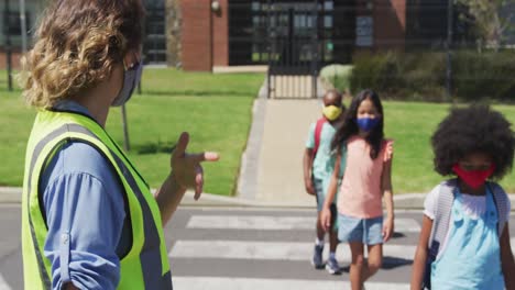 female woman wearing hi vis vest helping group of kids wearing face masks to cross the road