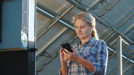 the woman uses a smartphone stands at the inverter under the panels of the house