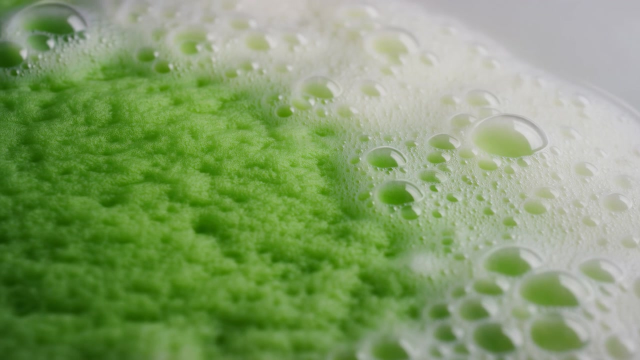 Schiuma con particelle verdi, nessuna azione osservata, in primo piano sulla schiuma, con texture di materiale schiumoso, da una prospettiva macro ravvicinata, con accenti bianchi e verdi.