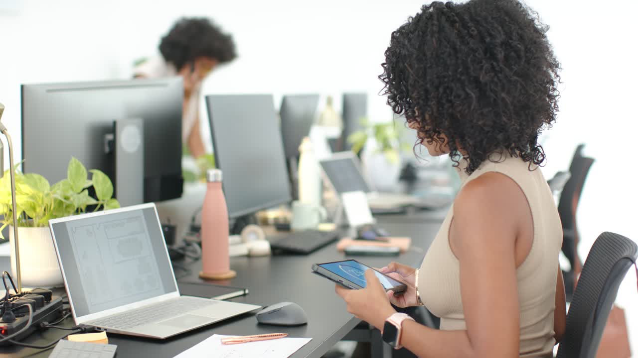 Vertical video: Holding tablet, phone, seated pro in tan top using it, checking PC for work at desk