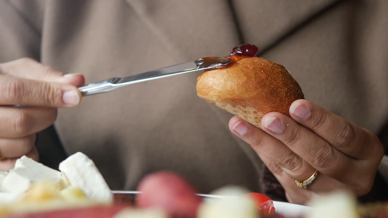Close-Up of Hands Spreading Jam on a Fresh Bread Roll