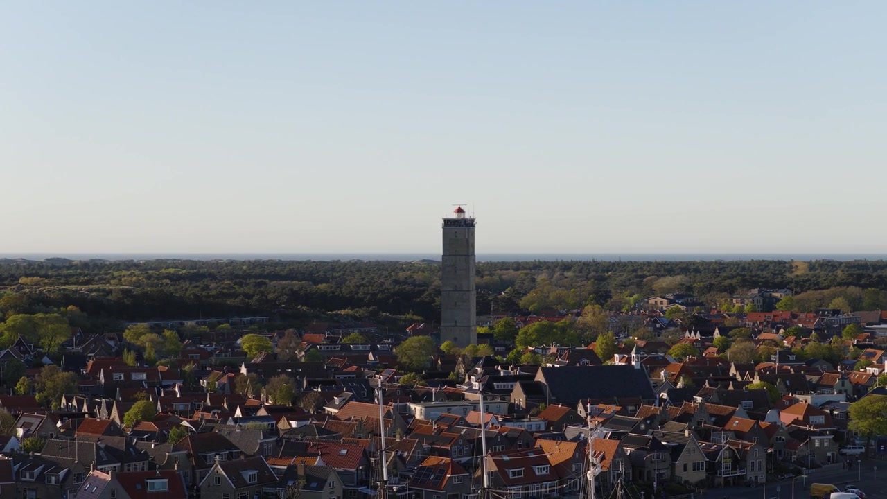 Faro di Brandaris a West-Terschelling, Terschelling, Frisia, Paesi Bassi, che rivela la storica città costiera e il paesaggio circostante del Mare dei Wadden, ripresa aerea all'indietro con drone.