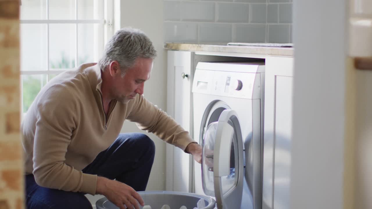 hombre caucásico feliz sosteniendo una canasta y lavando la ropa en la cocina