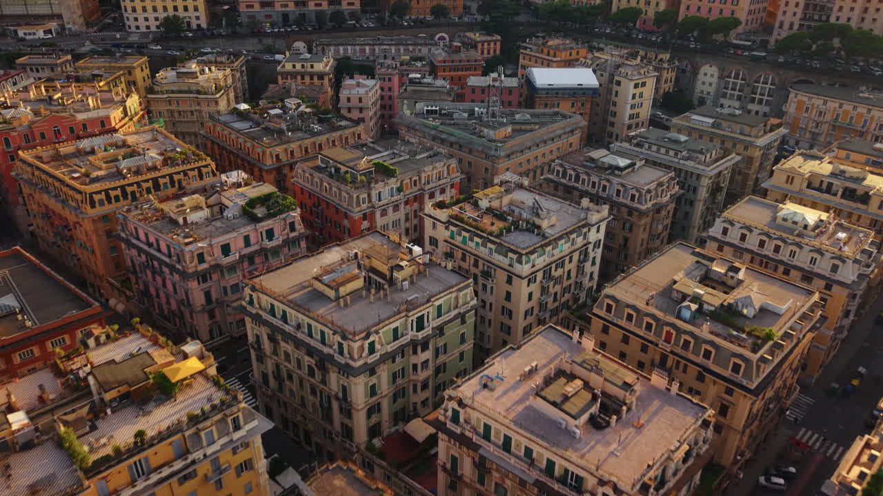Drone moves forward over Genoa rooftops, some greened, showing symmetrical streets at sunset