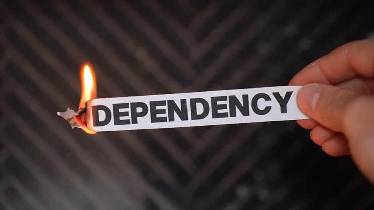 Hand burns a paper label reading “CODEPENDENCY,” symbolizing breaking unhealthy attachment—setting boundaries, independence, and relationship recovery. Dark background with copy space
