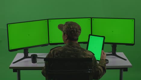 back view of asian man soldier working with tablet and multiple computer monitor with mock up green screen in green screen studio