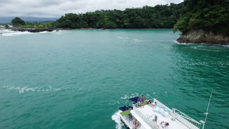 Muñeca-Aérea-En-Un-Barco-Navegando-En-El-Mar-Turquesa-Cerca-De-La-Costa-De-La-Colina-Cubierta-De-Selva-Verde,-Parque-Nahomi,-Costa-Rica