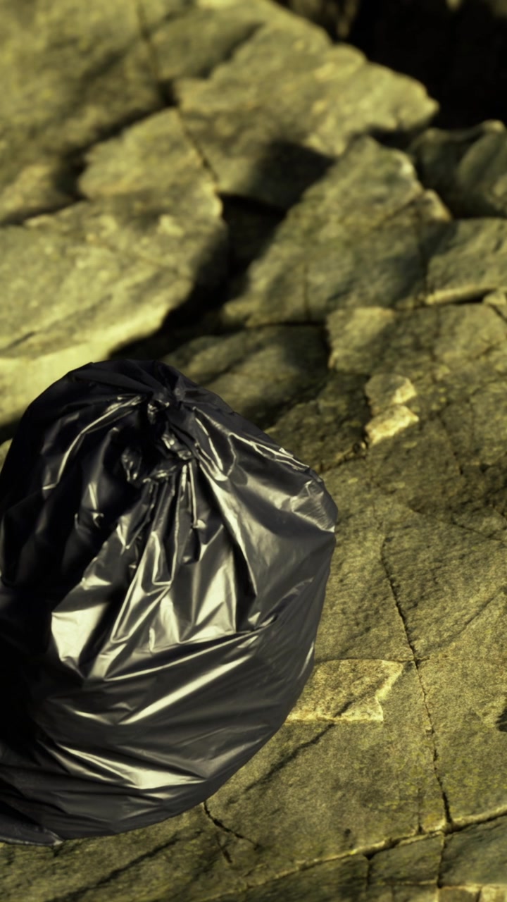 Un sacchetto di immondizia su una superficie rocciosa vicino alla riva, in un luogo soleggiato.