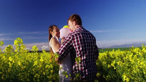 romantic couple holding colorful balloons and embracing each other in mustard field