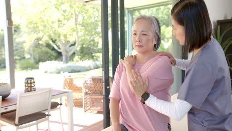 Physical therapist assisting senior asian woman with shoulder exercise at home