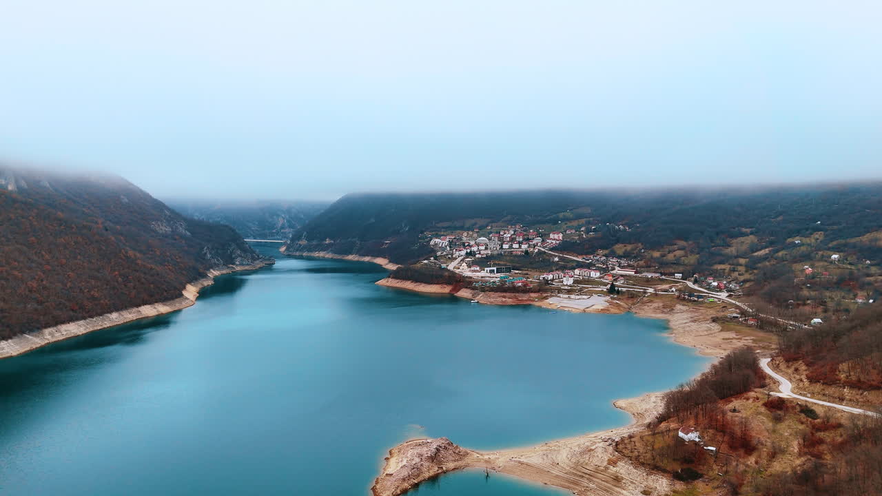 Luchtpanorama van het stadje Plužine aan de oever van het Piva-meer. Breed shot van een kleine bergnederzetting naast blauw water, omringd door mistige heuvels