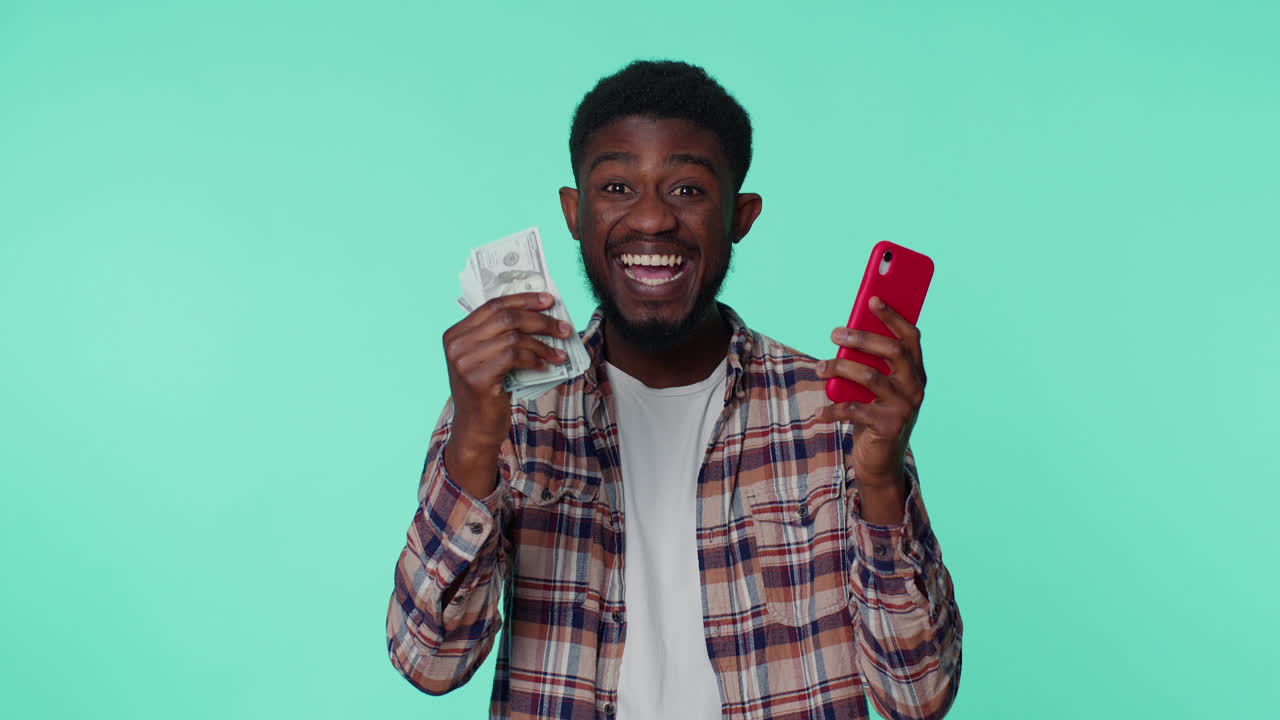 Happy african american man mobile phone display sincerely rejoicing win, receiving money dollar cash