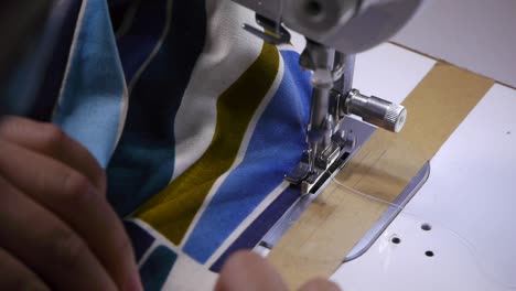 primer plano de las manos empujando tela con patrones a través de una máquina de coser para agregar puntadas en el borde de la tela