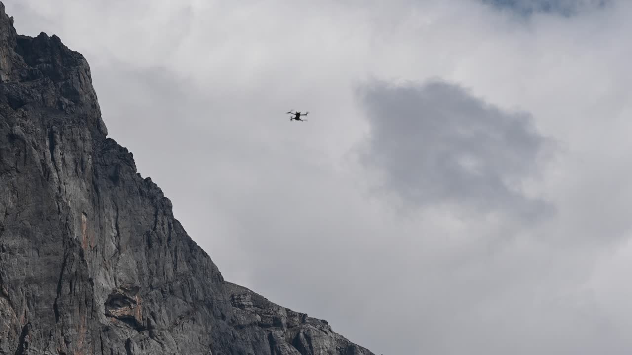 드론 dji mini 3 pro는 공중에 떠 있고 움직이지 않고 흐린 하늘과 스위스의 바위 산 정상 근처에서 분리됩니다.