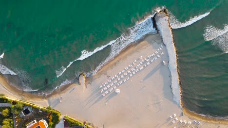 drone top-down view of sea waves and sandy beach with sunbeds at robinson beach on the bulgarian black sea coast