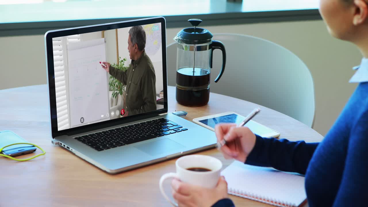 Kaukasisk kvindelig studerende bruger bærbar computer på videoopkald med mandlig lærer og tager noter.