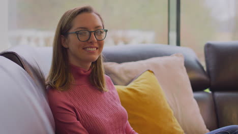 Porträt-Einer-Lächelnden-Frau-Mit-Brille,-Die-Es-Sich-Zu-Hause-Auf-Dem-Sofa-Gemütlich-Macht