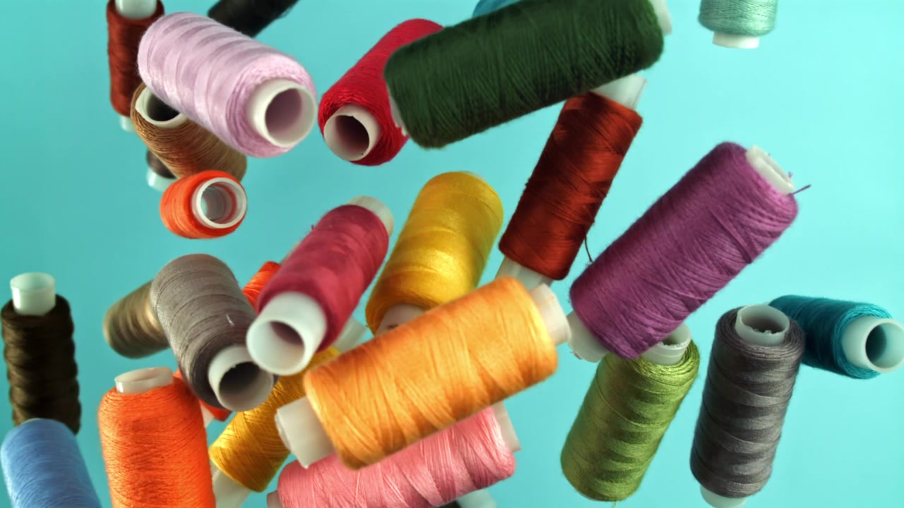 Colorful Sewing Threads Falling in Slow Motion on Blue Background