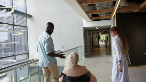 assisting woman in wheelchair, african american man and woman walking in modern office hallway