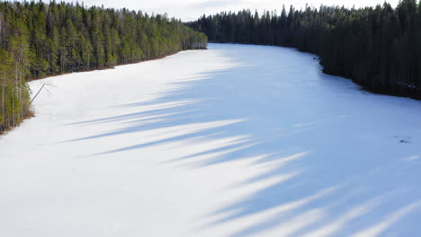 drone shot of remote narrow icy lake and nice shadows from spruce trees on the ice