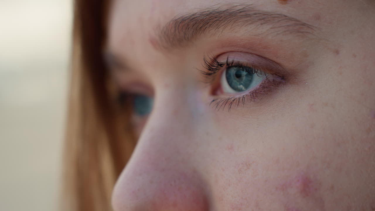 Primo piano di acne giovanile vicino all'occhio di una giovane adolescente, aspirante pittrice in pausa al tramonto, luce naturale soffusa, iride blu, imperfezioni e lentiggini visibili, residuo di mascara, espressione calma e introspettiva, bokeh all'aperto, pelle al naturale.