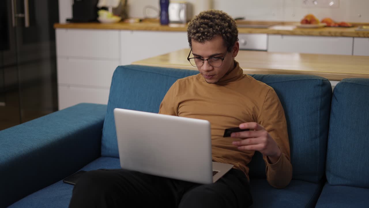 Young man buying online uses a laptop and a credit card on sofa home