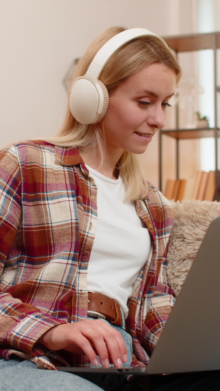 Smiling woman enjoying music on laptop at home with wireless headphones moving gently to rhythm