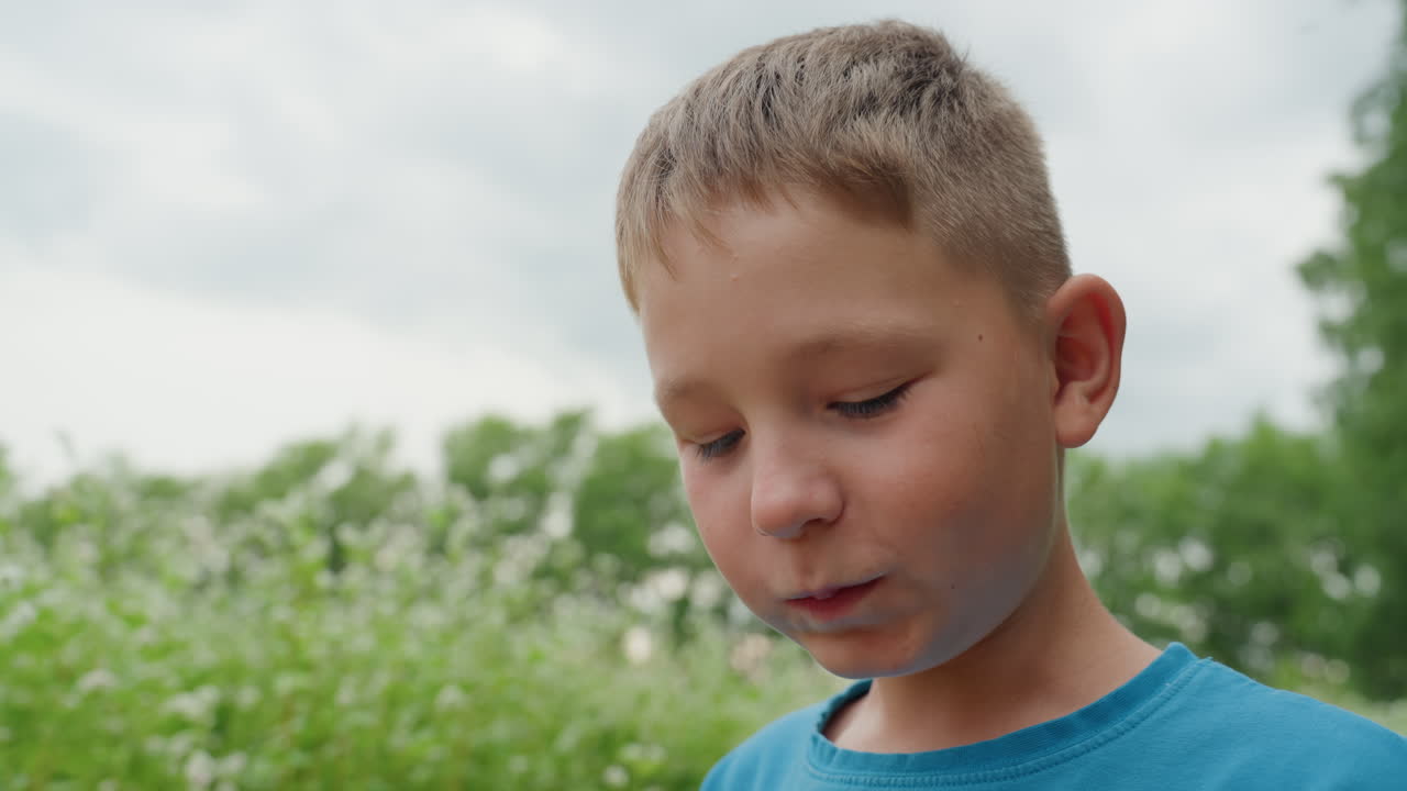 초원에서 음료를 마시는 백인 소년, 흐린 하늘과 야생화, 유리병을 가까이 든 채 맛을 음미하며 생각에 잠긴 표정, 뒷마당 피크닉 장면, 풋풋한 순수함과 부드러운 바람, 고요함