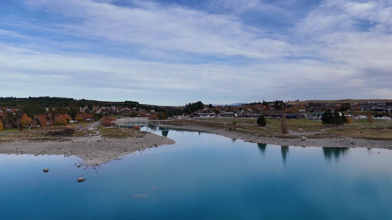 Drone footage captures Lake Tekapo's serene waters and surrounding landscape under a clear sky, showcasing natural beauty and tranquility