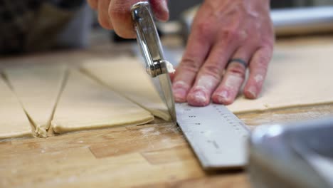 dough rolls up on pastry wheel cutter as baker precisely measures and cuts dough into triangles for croissants, slow motion close up 4k