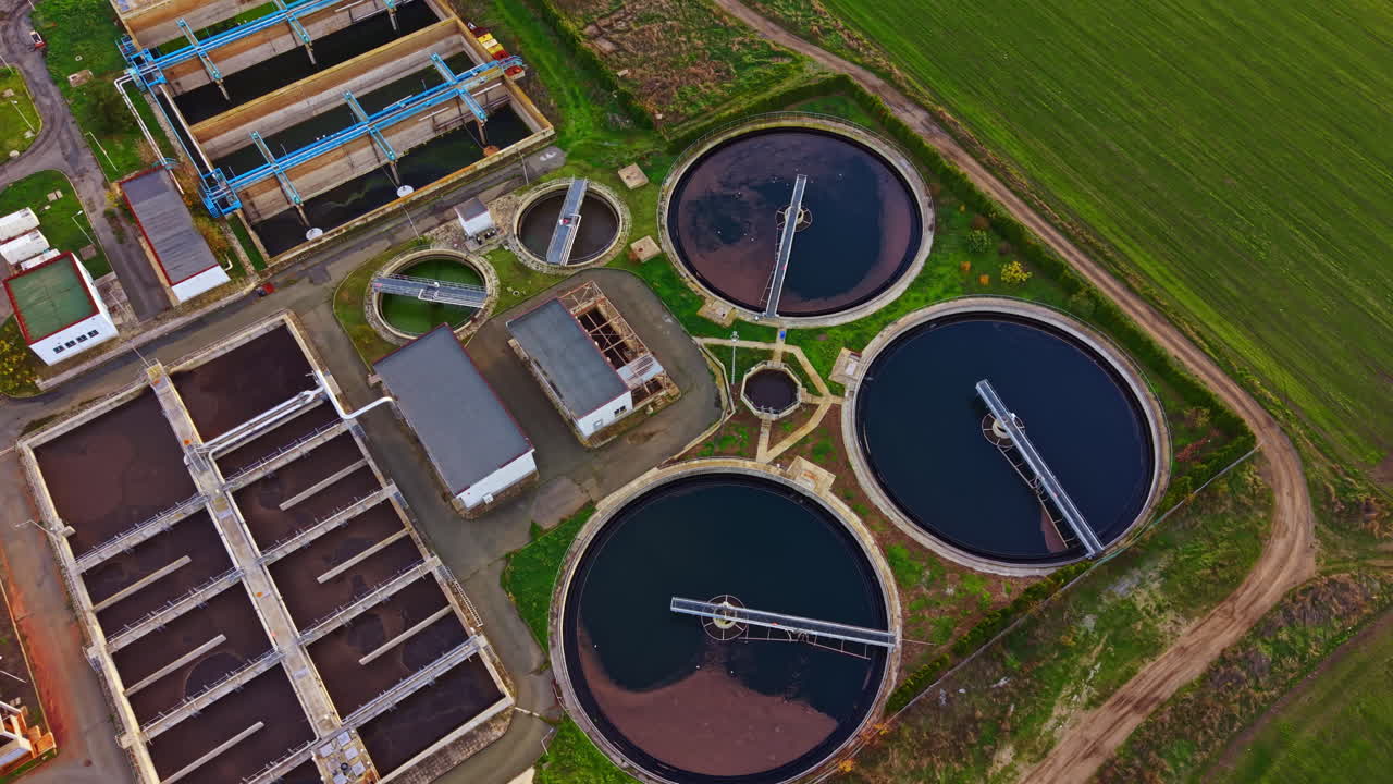 Water treatment facility processing wastewater in a rural area surrounded by greenery and fields during sunny weather