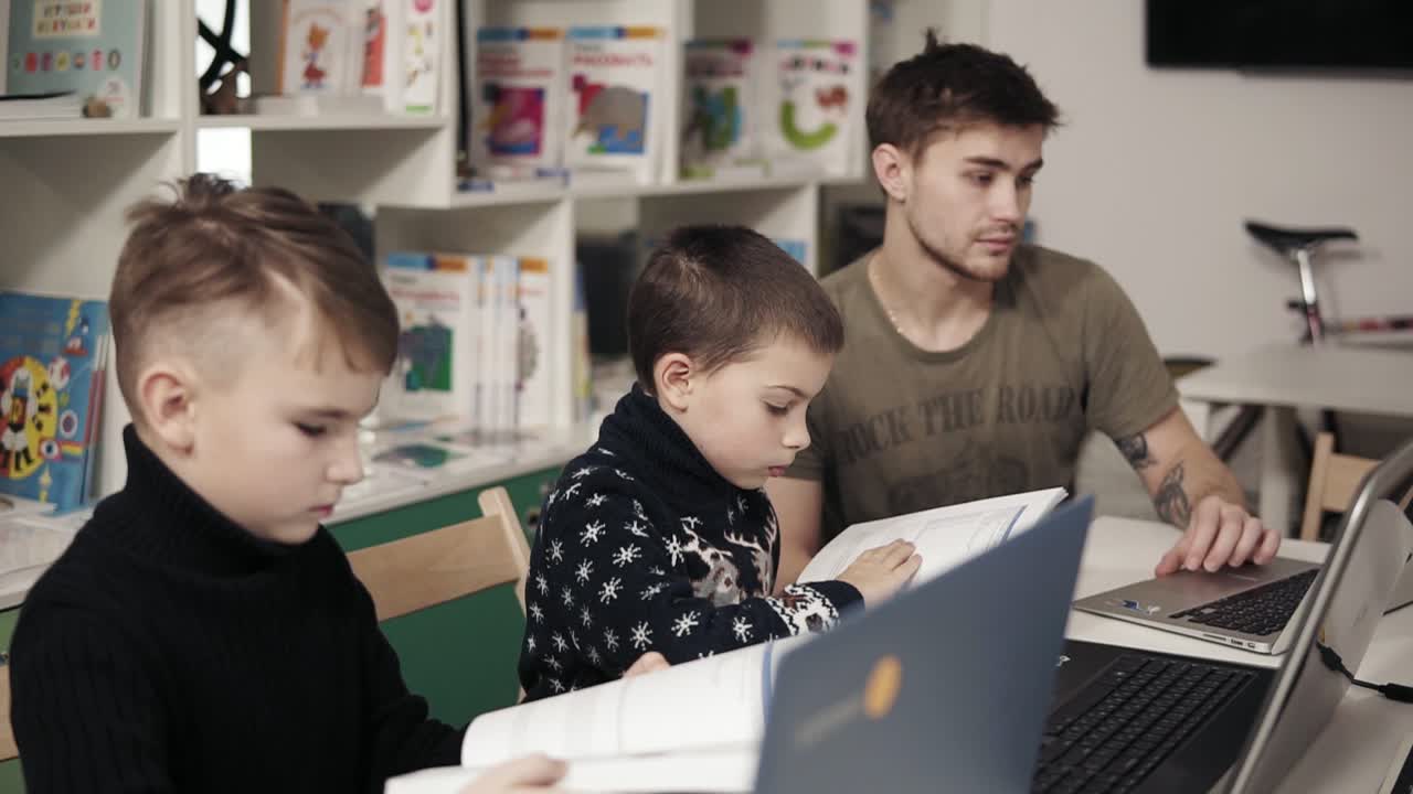 dos niños pequeños están leyendo libros relacionados con computadoras y programación. proceso educativo. un joven y atractivo maestro les está explicando cómo funcionan los aparatos.