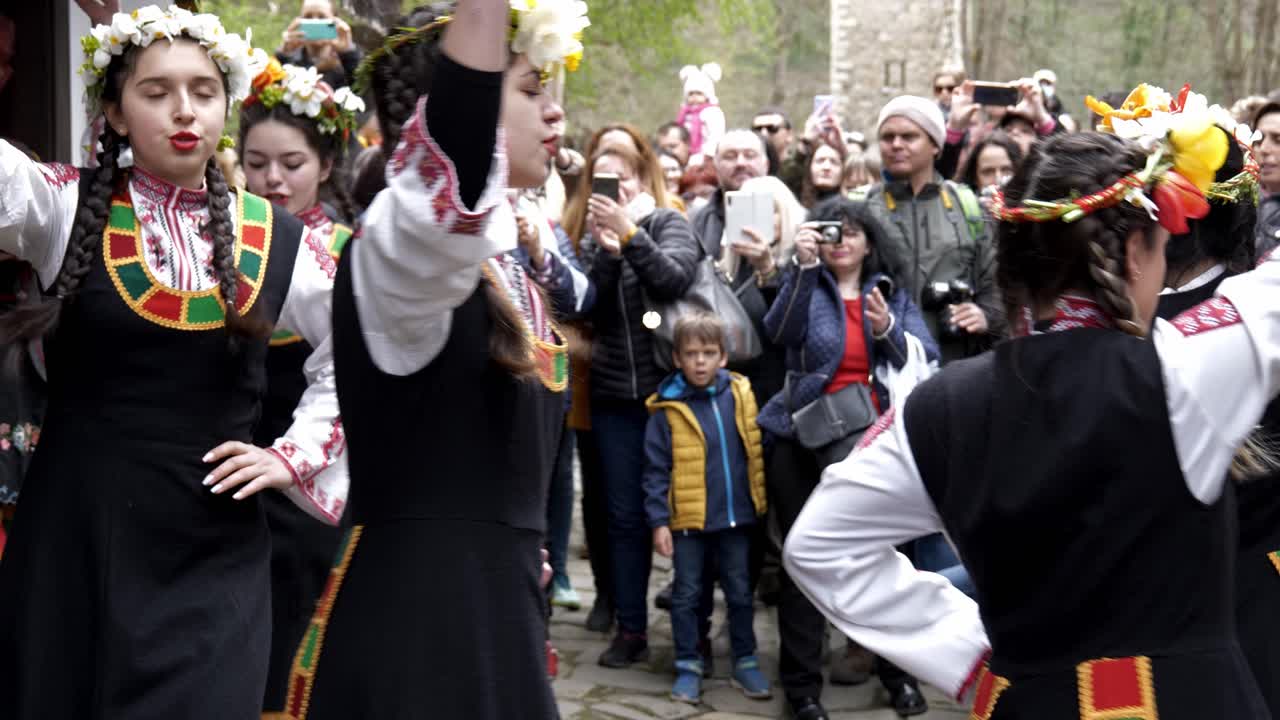 Pretty, Bulgarian girls in colourful traditional dress perform Easter time ritual dance in front of happy crowds.slow motion