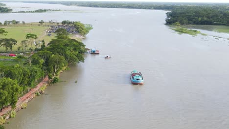 Vista-Aérea-Hacia-El-Lecho-Del-Río-Con-Cruceros-En-Barco-Cerca-De-La-Orilla-Boscosa,-Bangladesh