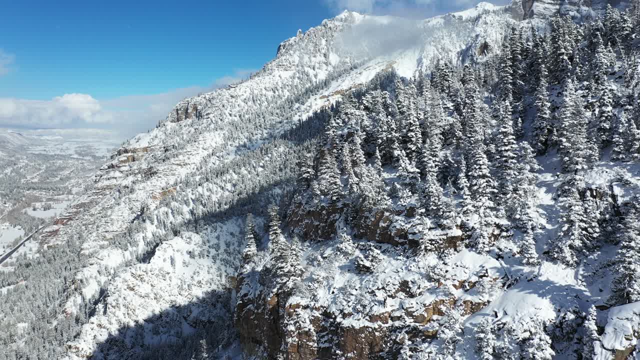 Sunny winter landscape, drone aerial view of snow capped mountain hills, peaks, clouds and conifer forest