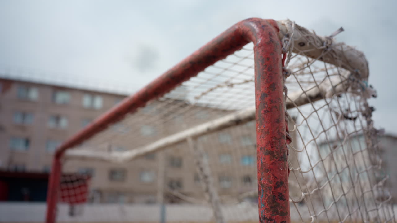 goalpost and net in city environment, soccer goal with buildings and overcast lighting in background, wideangle view of soccer goal surrounded by urban development under cloudy skies