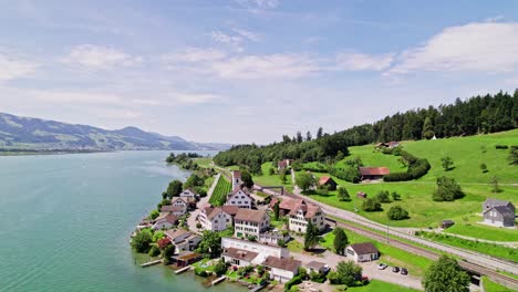 aerial orbit shot showing idyllic village named bollingen in front of idyllic lake and green hill scenery in background, switzerland