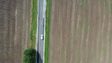 Aerial-shot-following-a-white-car-driving-on-a-2-lane-road