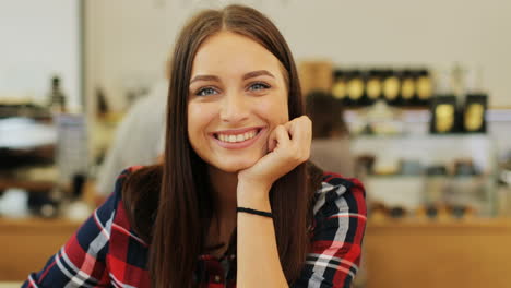 vista de cerca de una mujer morena con el pelo largo sonriendo a la cámara sentada en una mesa en un café