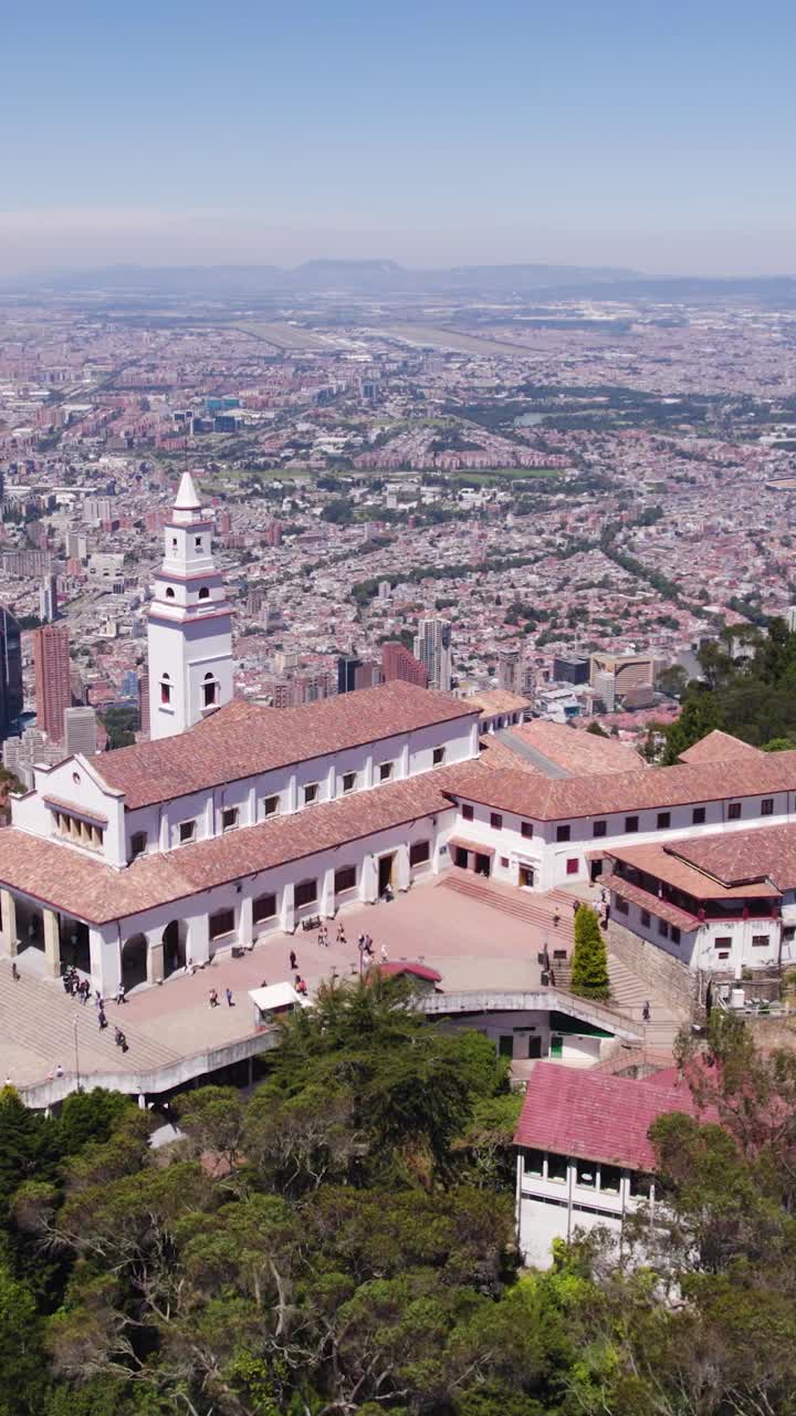 Aerial view of the Monserrate Sanctuary, a neocolonial church located on top of Monserrate mountain, with Bogota cityscape in background. Vertical Video