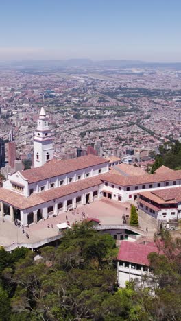 aerial view of the monserrate sanctuary, a neocolonial church located on top of monserrate mountain, with bogota cityscape in background. vertical video