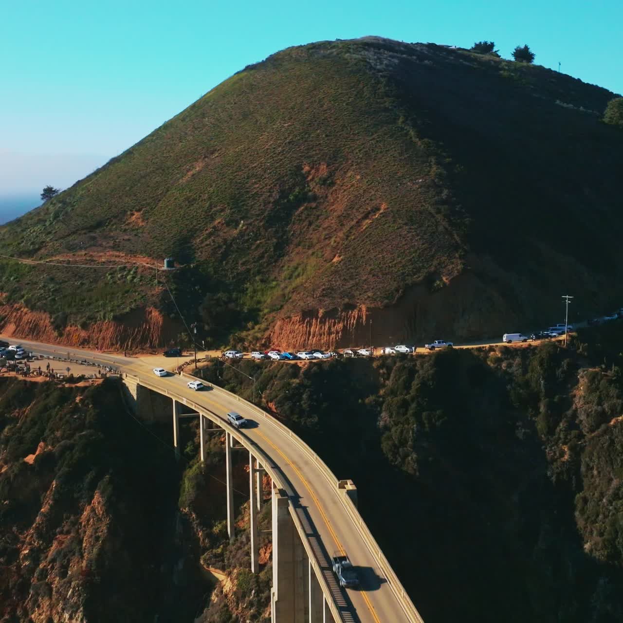 Busy road around the rugged mountain passing into the beautiful arched bridge over the gap in the rocks. Blue skies at backdrop. Top view
